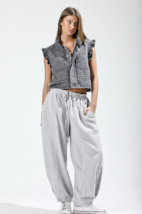 Woman wearing a sleeveless denim jacket and gray pants on a white background