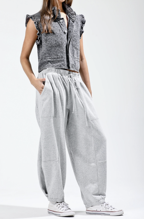 Person wearing a sleeveless gray top with ruffled details and light gray pants on a white background
