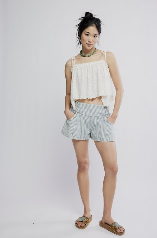 Woman wearing a white top and striped shorts on a plain background