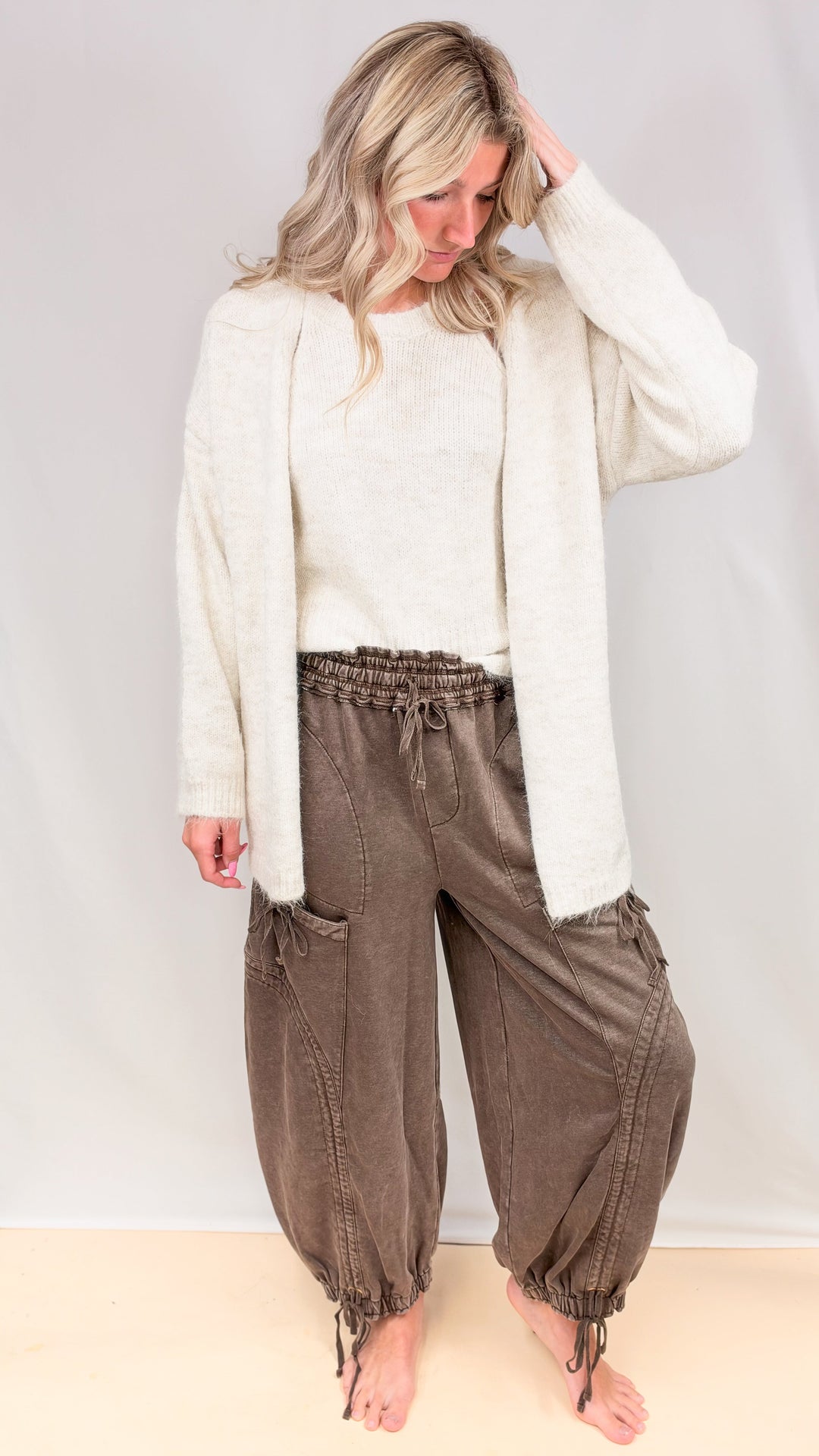 Woman wearing brown balloon pants with drawstrings and cardigan on plain background