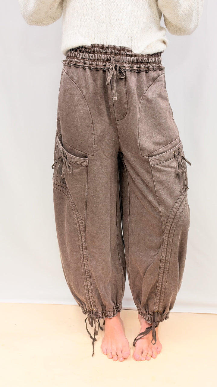 Woman wearing brown balloon pants with drawstring details and beige top on plain background