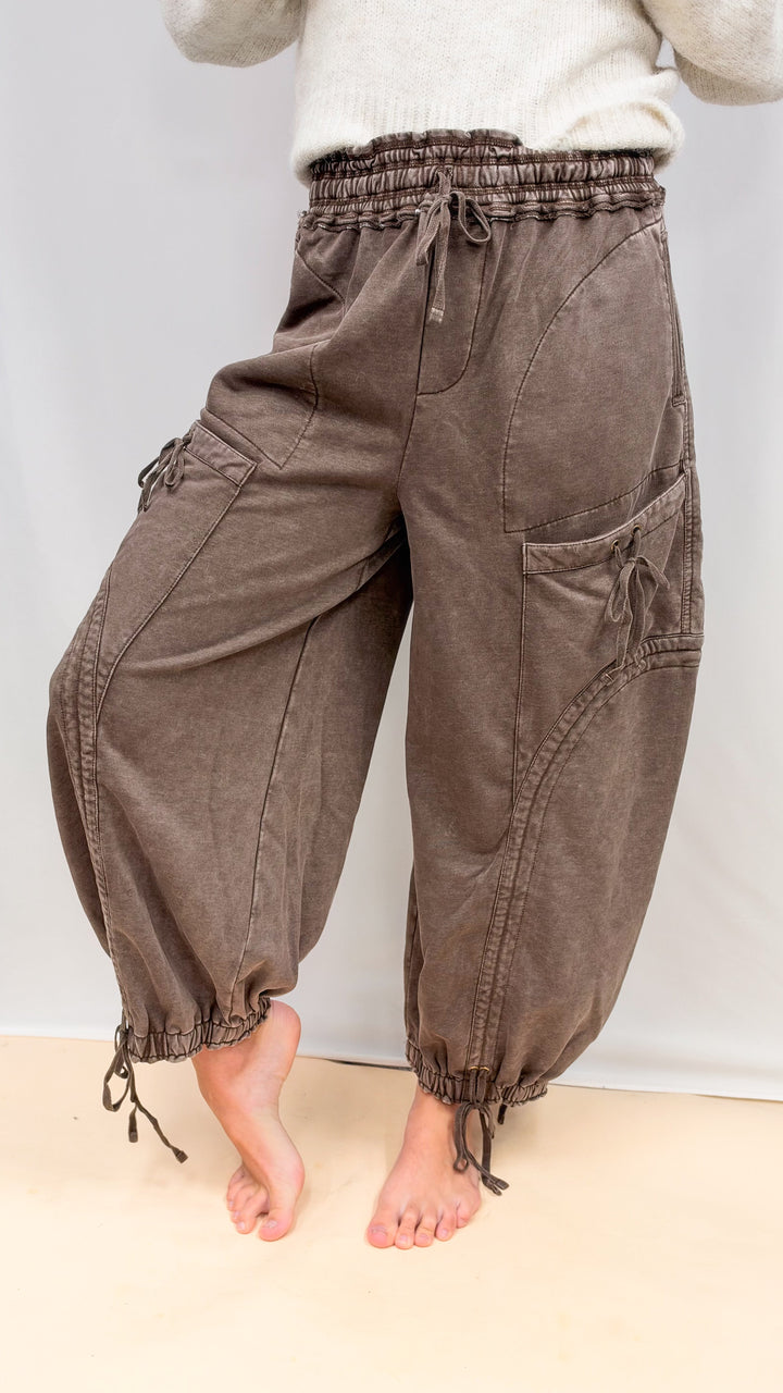 Woman wearing brown balloon pants with drawstring details and beige top on plain background