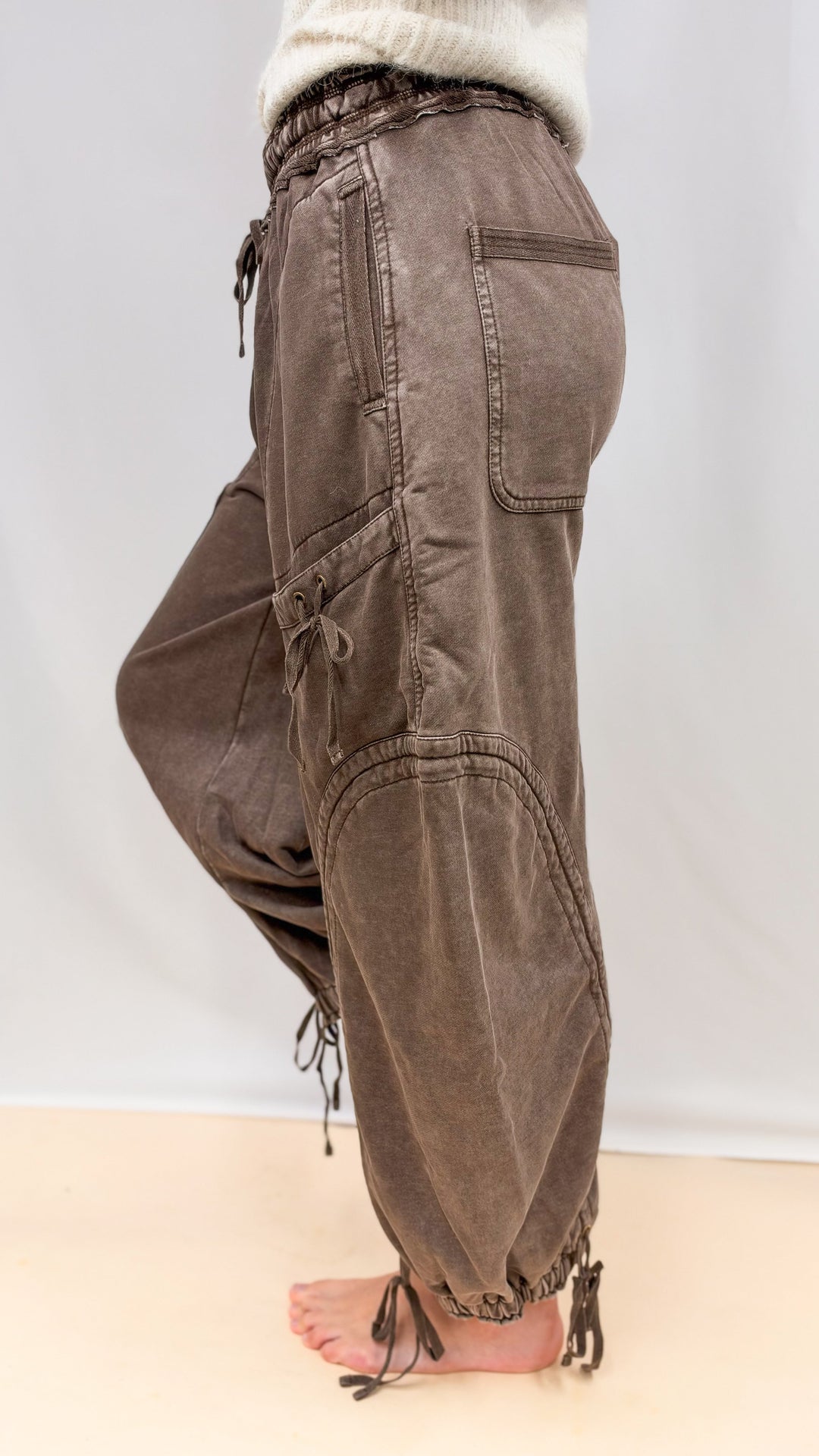 Woman wearing brown balloon pants with drawstring details and beige top on plain background
