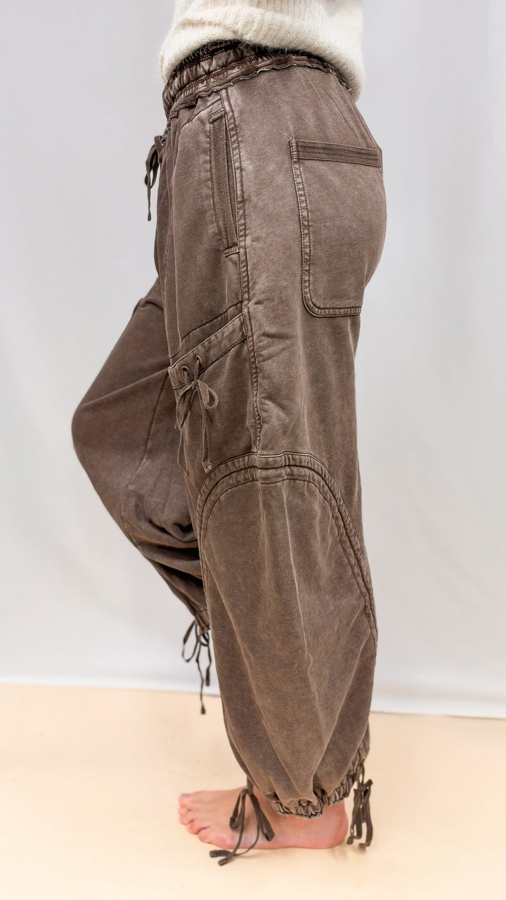 Woman wearing brown balloon pants with drawstring details and beige top on plain background