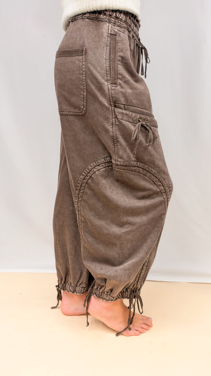 Woman wearing brown balloon pants with drawstring details and beige top on plain background