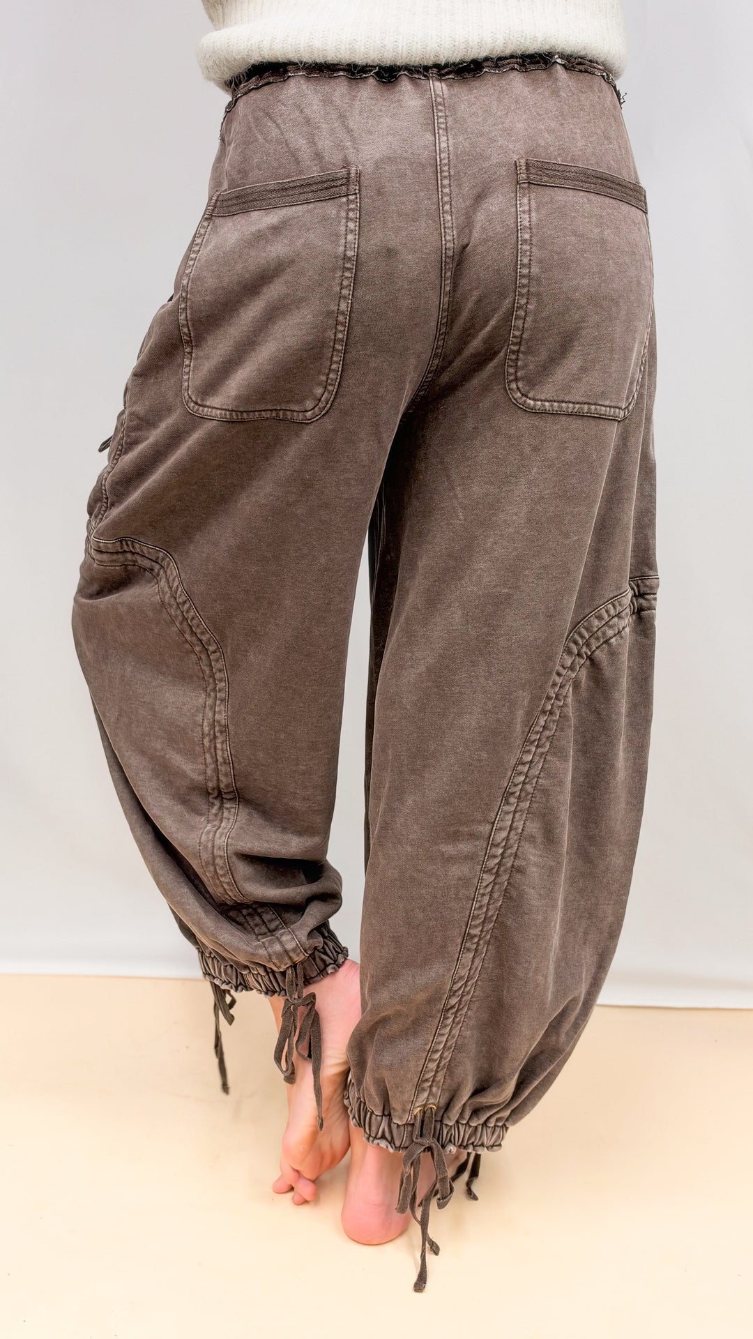 Woman shown from back wearing brown balloon pants with drawstring details on plain background