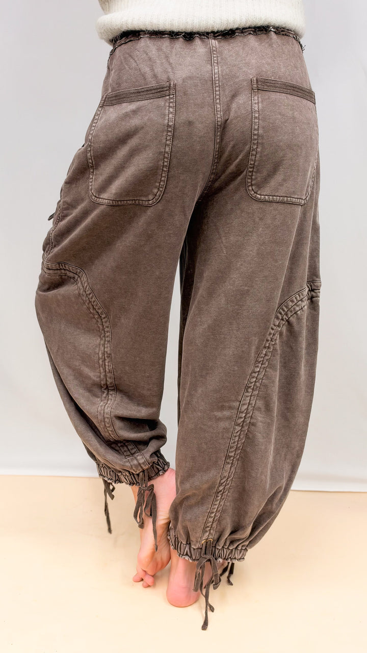 Woman shown from back wearing brown balloon pants with drawstring details on plain background
