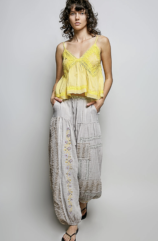 Woman wearing a yellow top and light gray patterned pants against a plain background