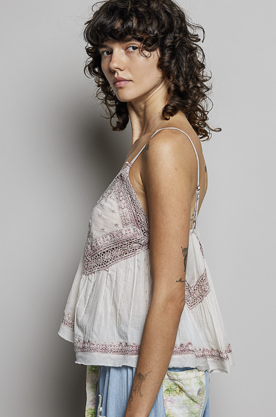 Woman wearing a white top with intricate patterns on a plain background