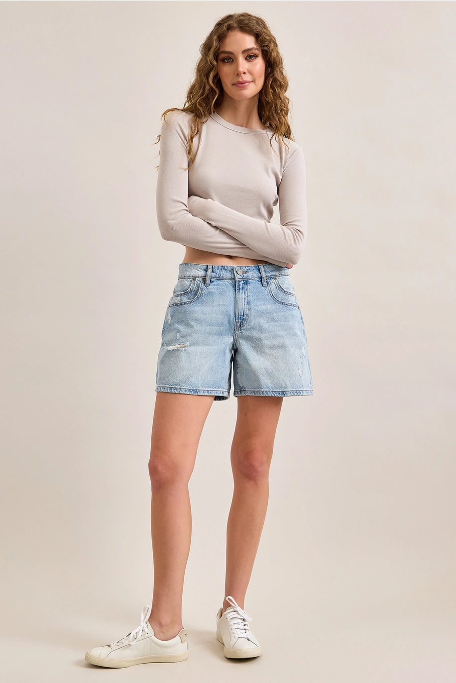 Woman wearing denim shorts and beige top on plain background