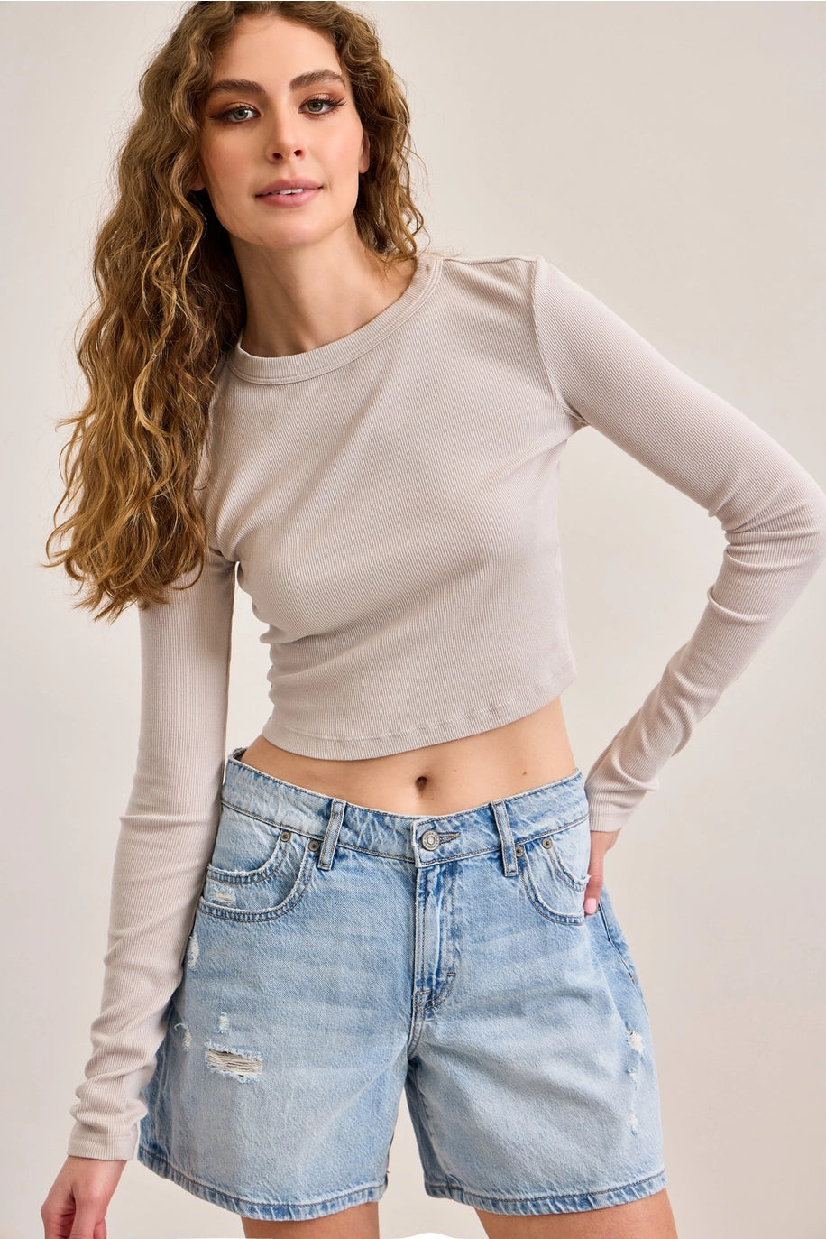Woman wearing denim shorts and beige top on plain background