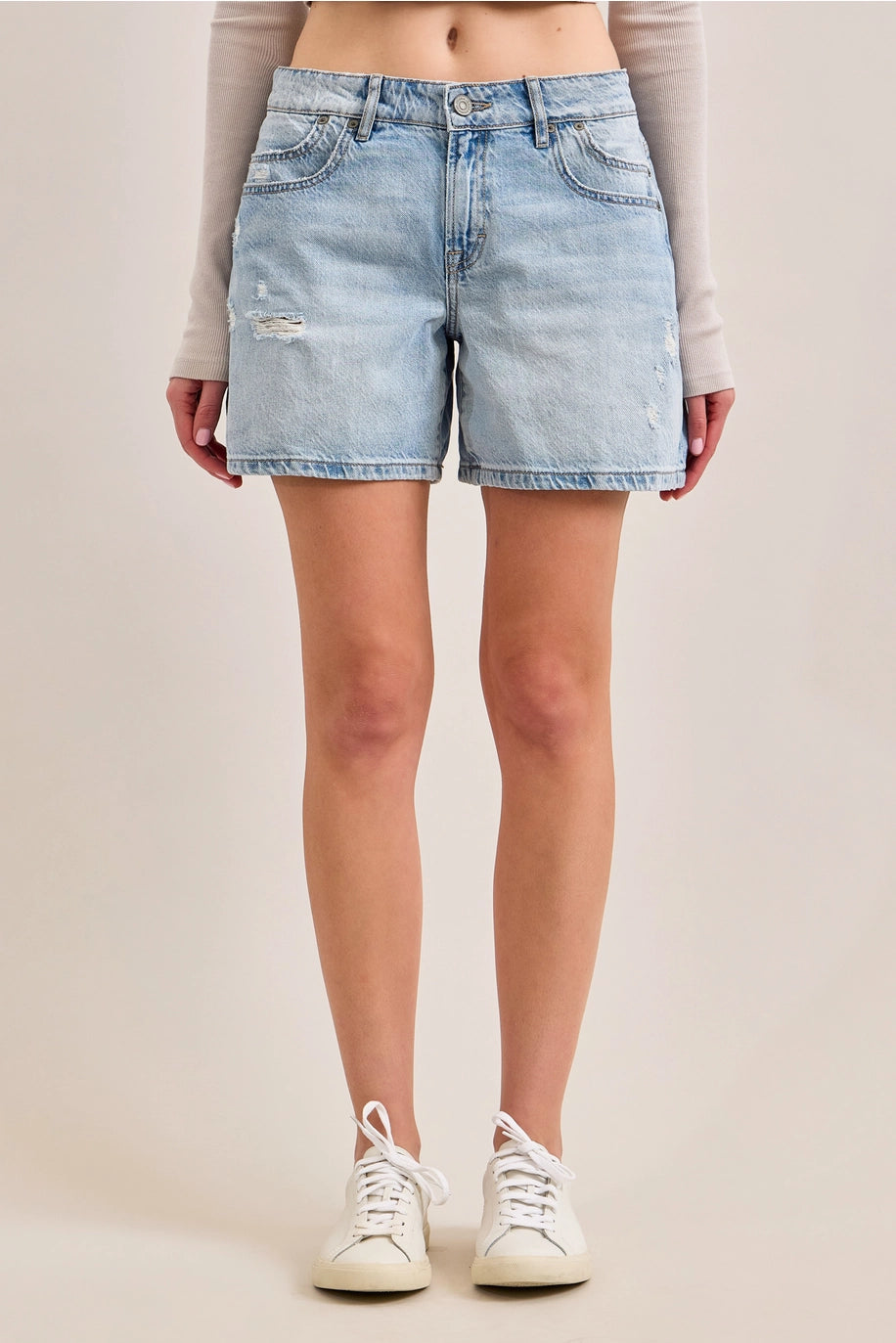 Woman wearing denim shorts and tennis shoes on plain background