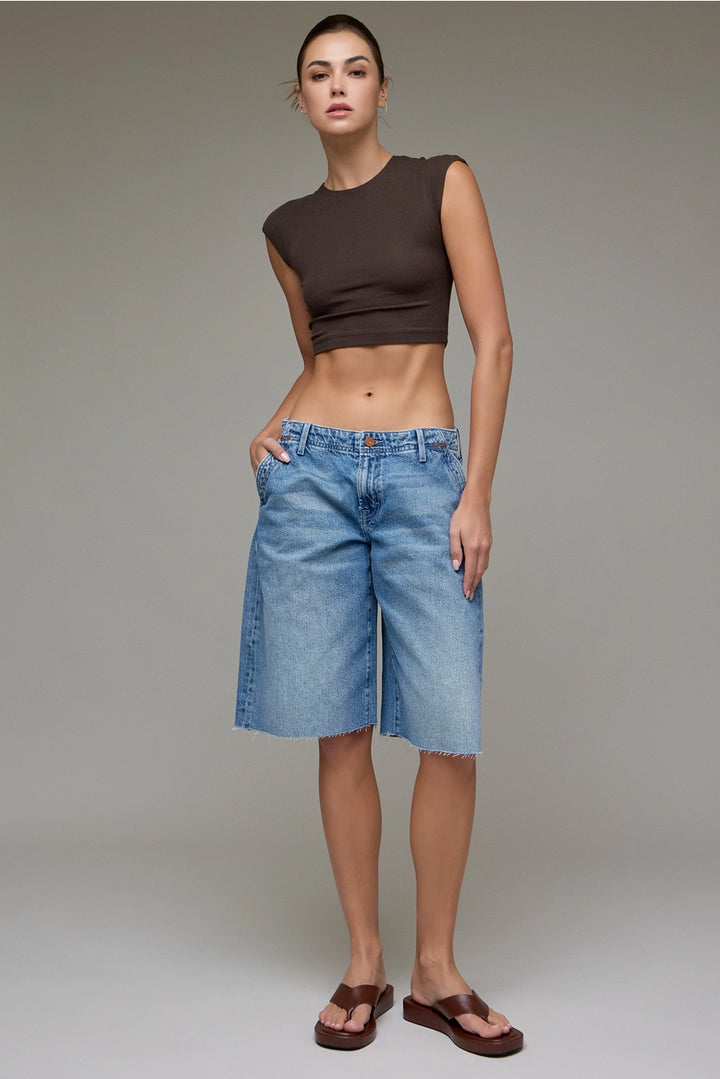 Woman wearing a brown sleeveless top and blue denim shorts on a plain background