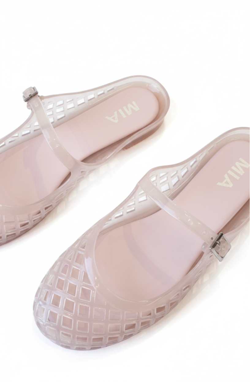 A pair of pale pink jelly shoes with a square cutout pattern and a transparent strap featuring a small silver buckle, resting on a white background. The brand name 'MIA' is printed on the insole.