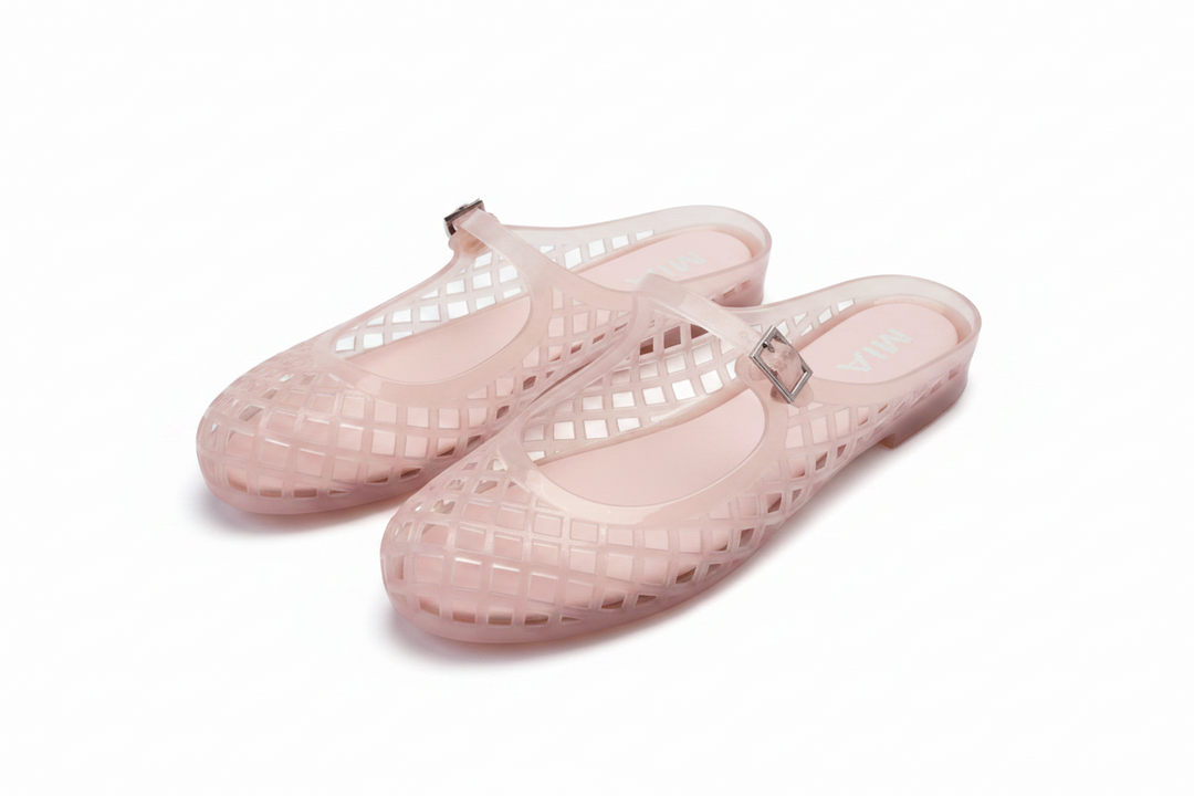A pair of translucent light pink jelly mule flats with a grid pattern and a small metallic square accent on the strap, resting on a white background.
