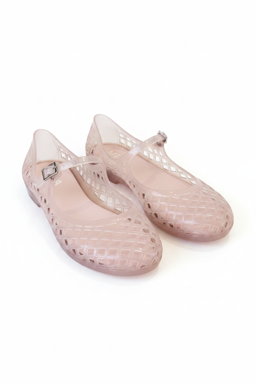 A pair of light pink jelly shoes with a grid-patterned cutout design and a small silver buckle on the strap, resting on white background