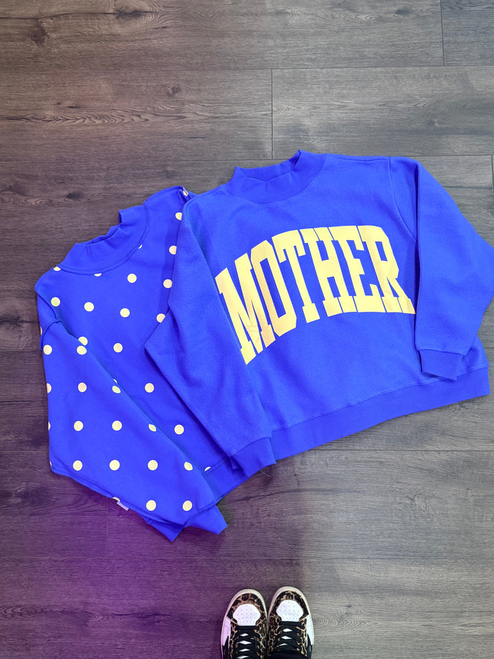 Blue mock neck sweatshirt with yellow "Mother" writing and yellow polka dots on a plain background