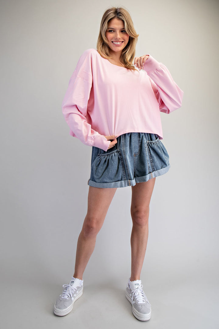 Woman wearing a pink sweater and denim shorts on a plain background