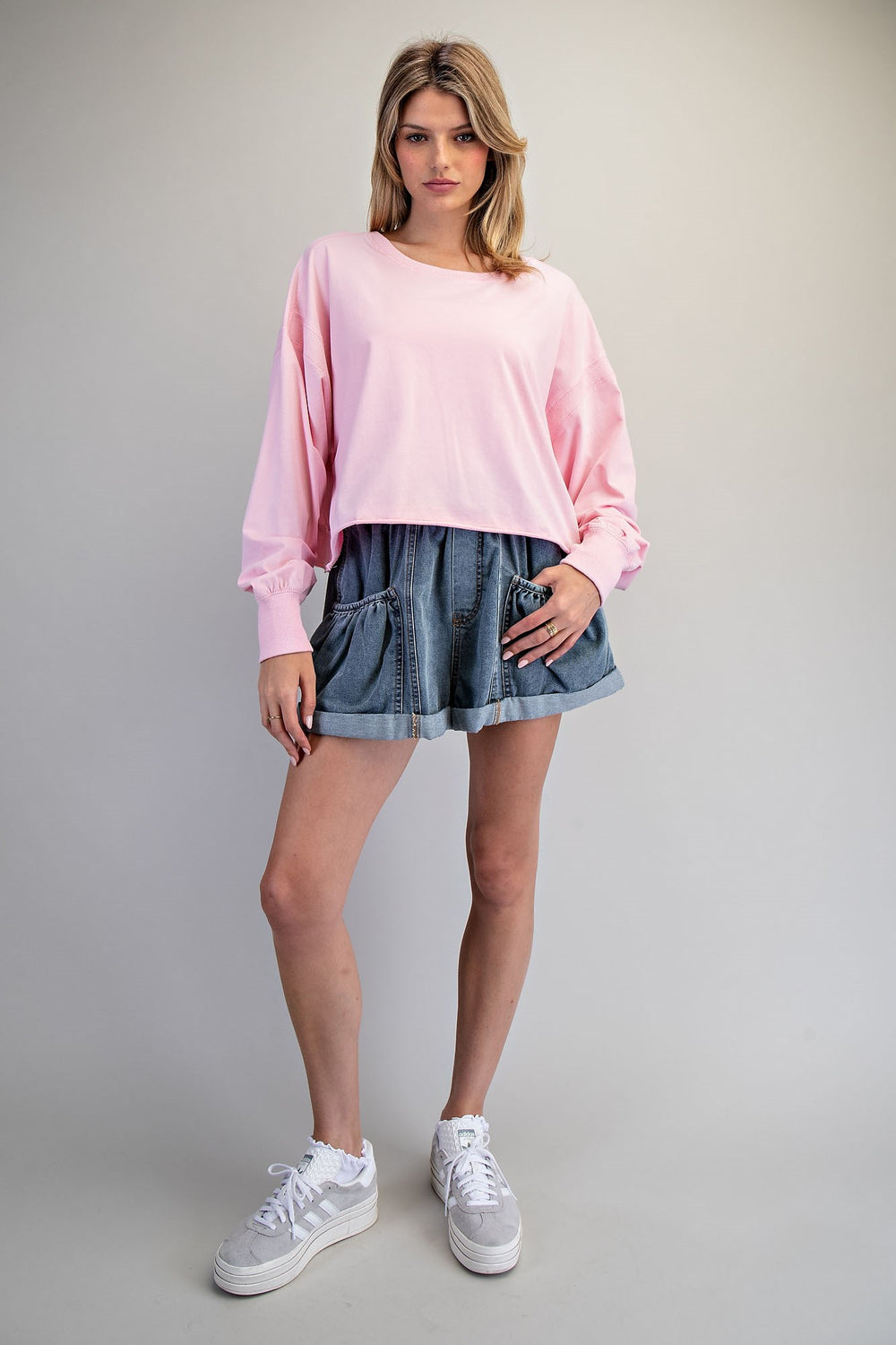 Woman wearing a pink sweater and denim skirt on a gray background