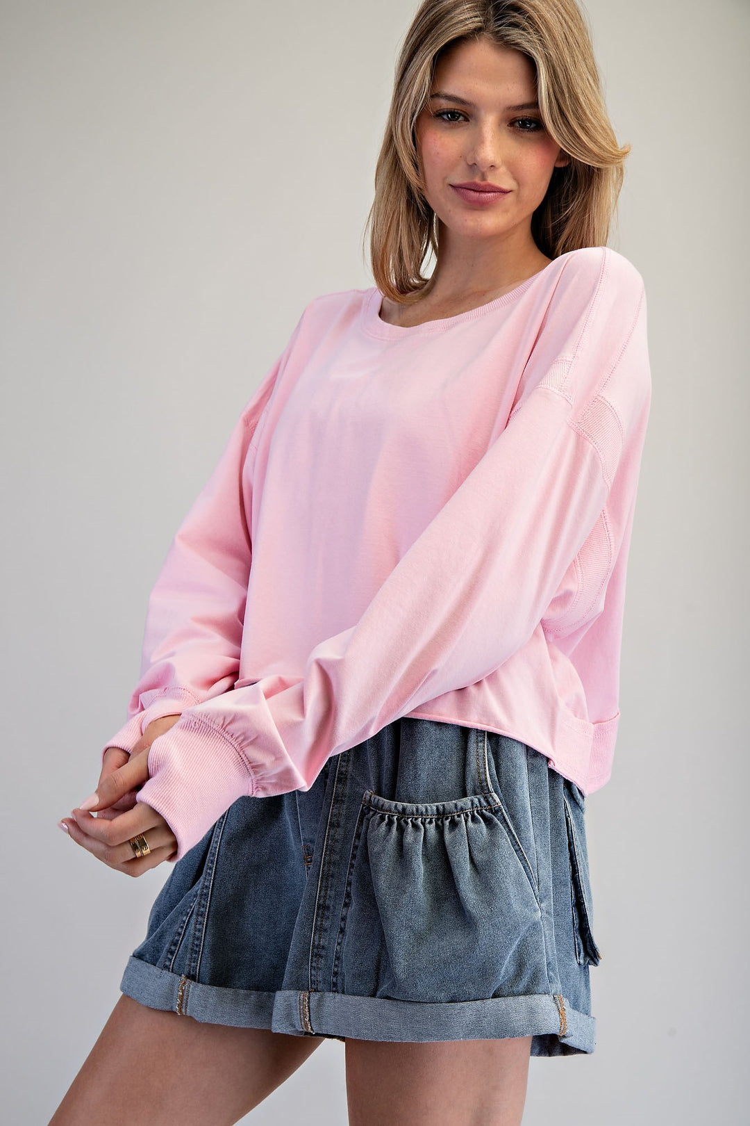 Woman wearing a pink blouse and denim shorts against a plain background