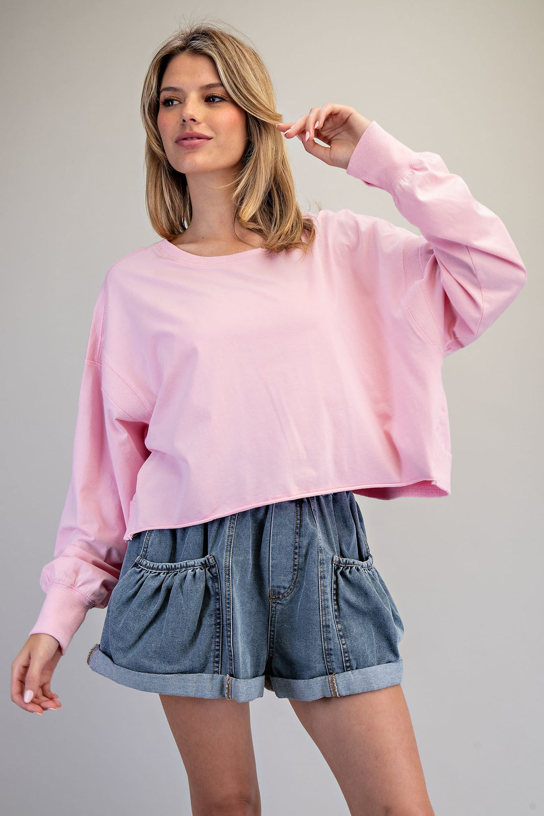 Woman wearing a pink sweatshirt and denim shorts on a plain background