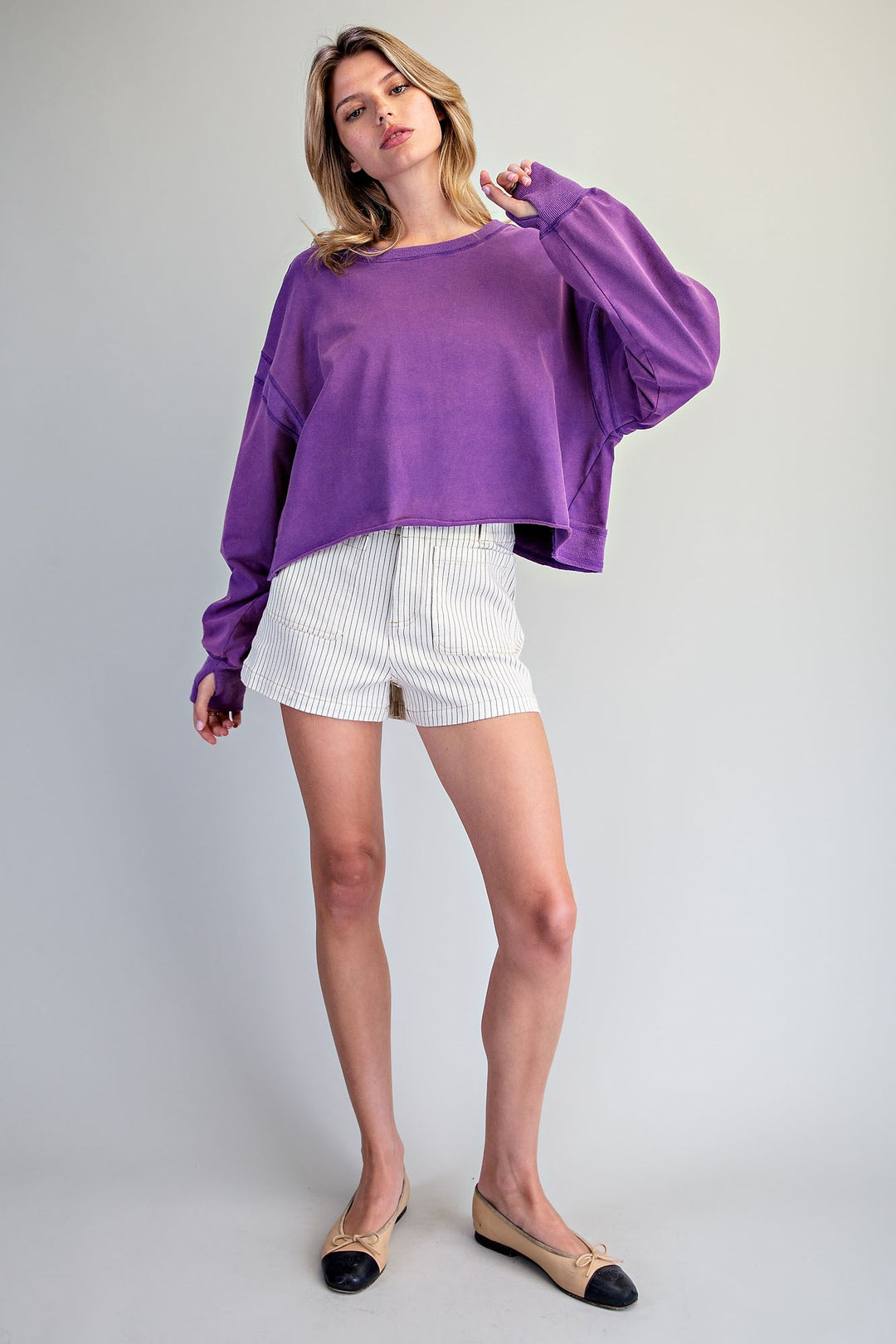 Woman wearing a purple top and white shorts on a plain background