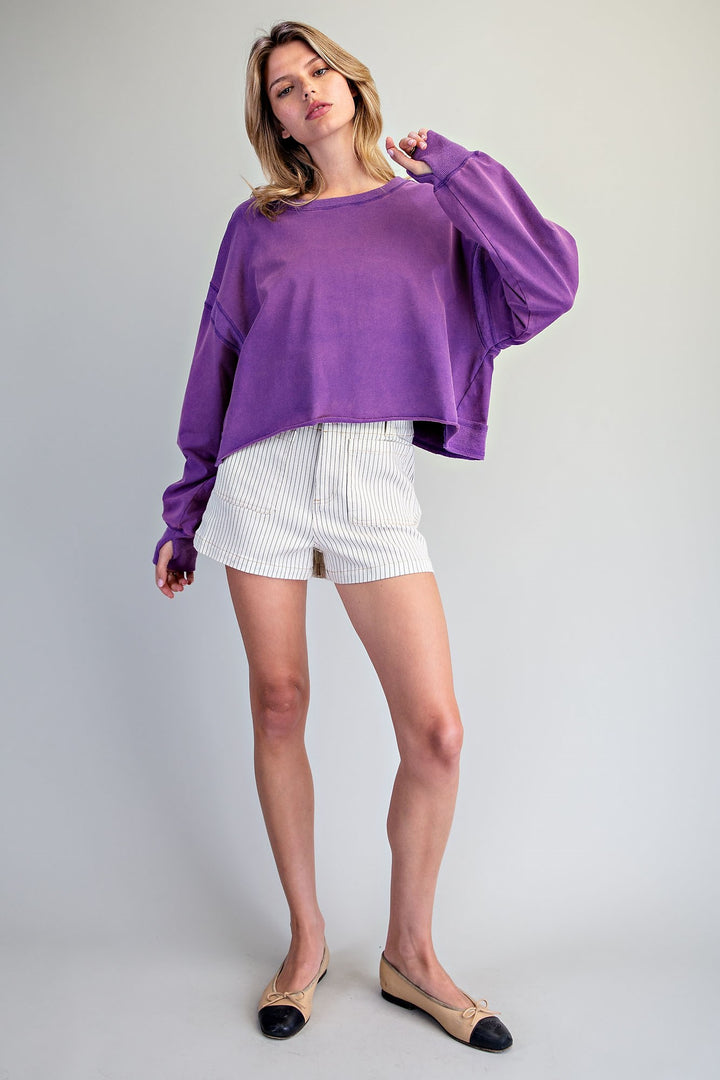 Woman wearing a purple top and white shorts on a plain background