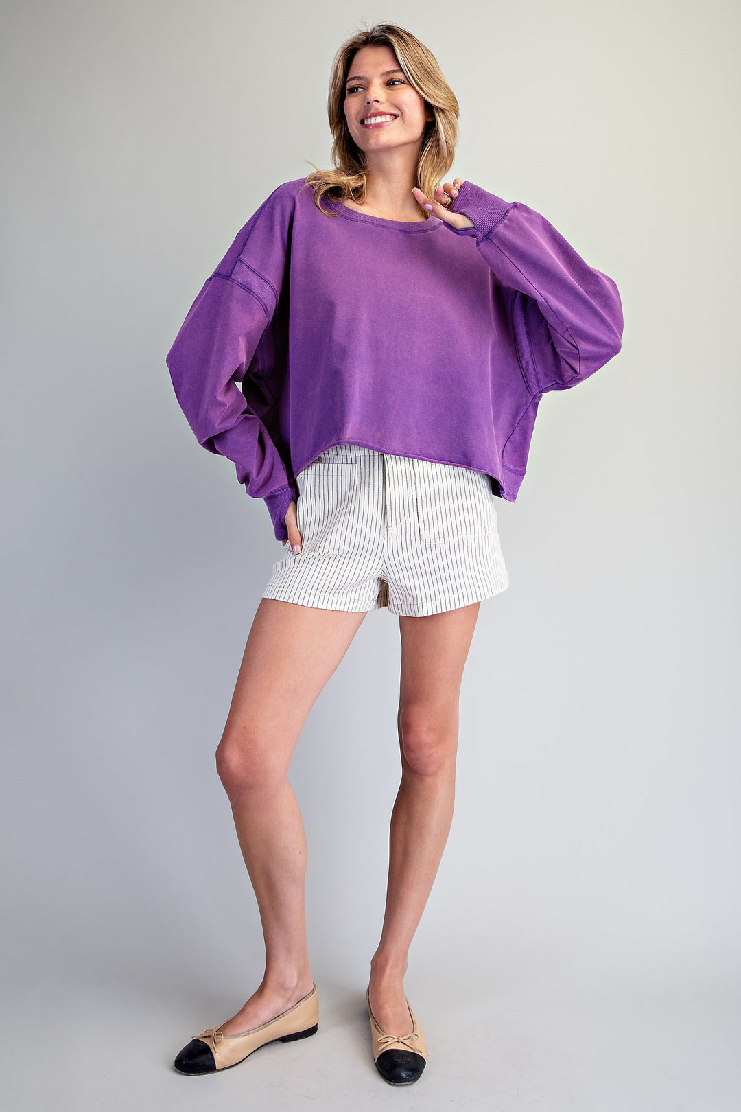 Woman wearing a purple sweater and white shorts on a plain background
