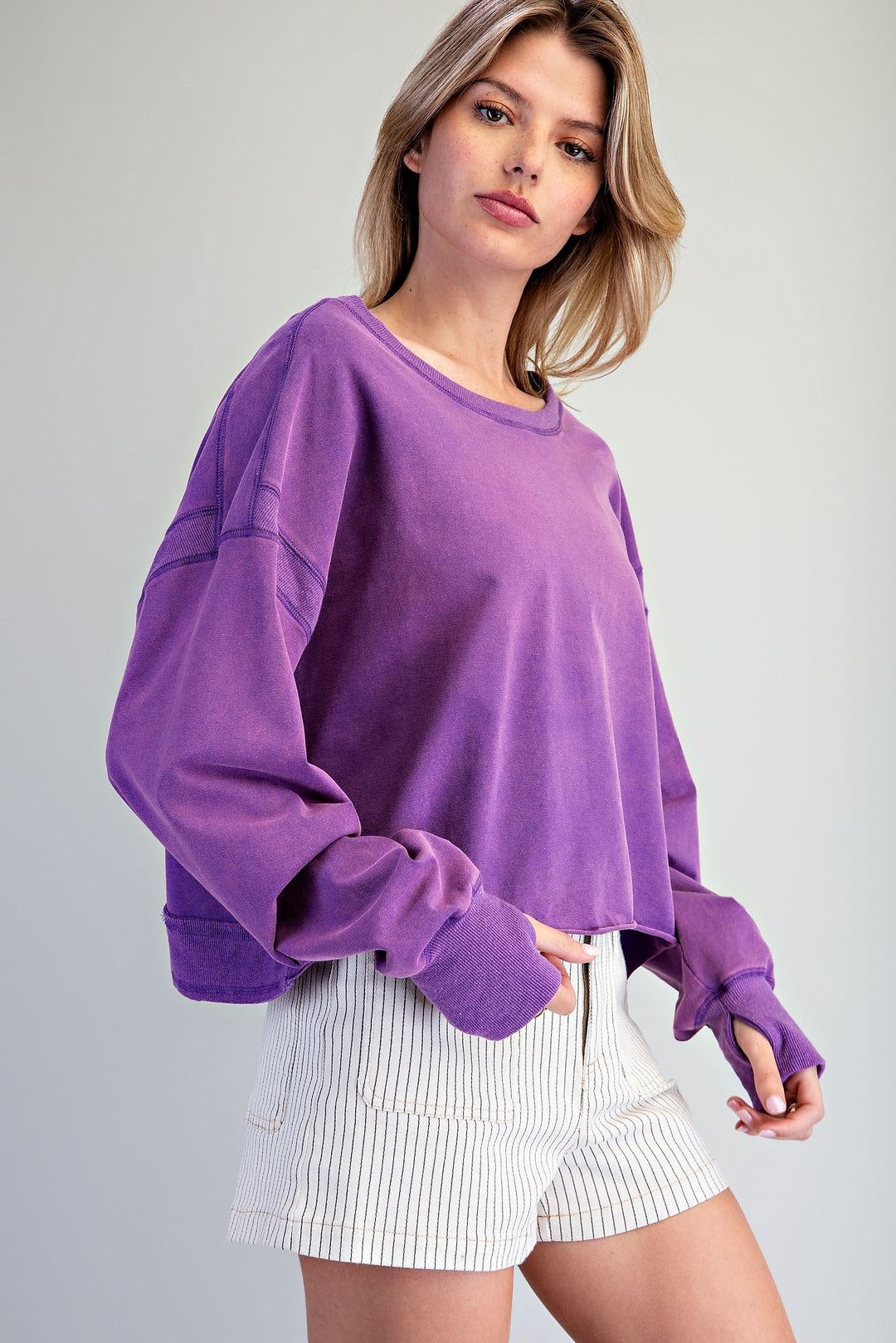 Woman wearing a purple oversized sweatshirt and white shorts on a gray background