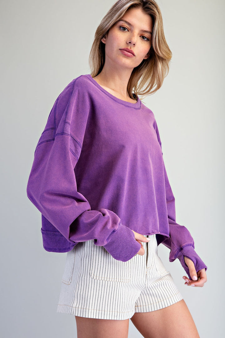 Woman wearing a purple oversized sweatshirt and white shorts on a gray background