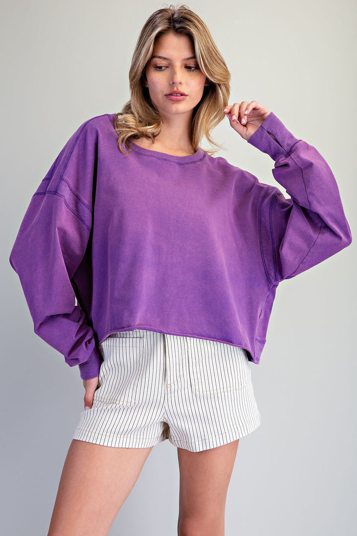 Woman wearing a purple oversized sweatshirt and white shorts with thin black stripes on a gray background