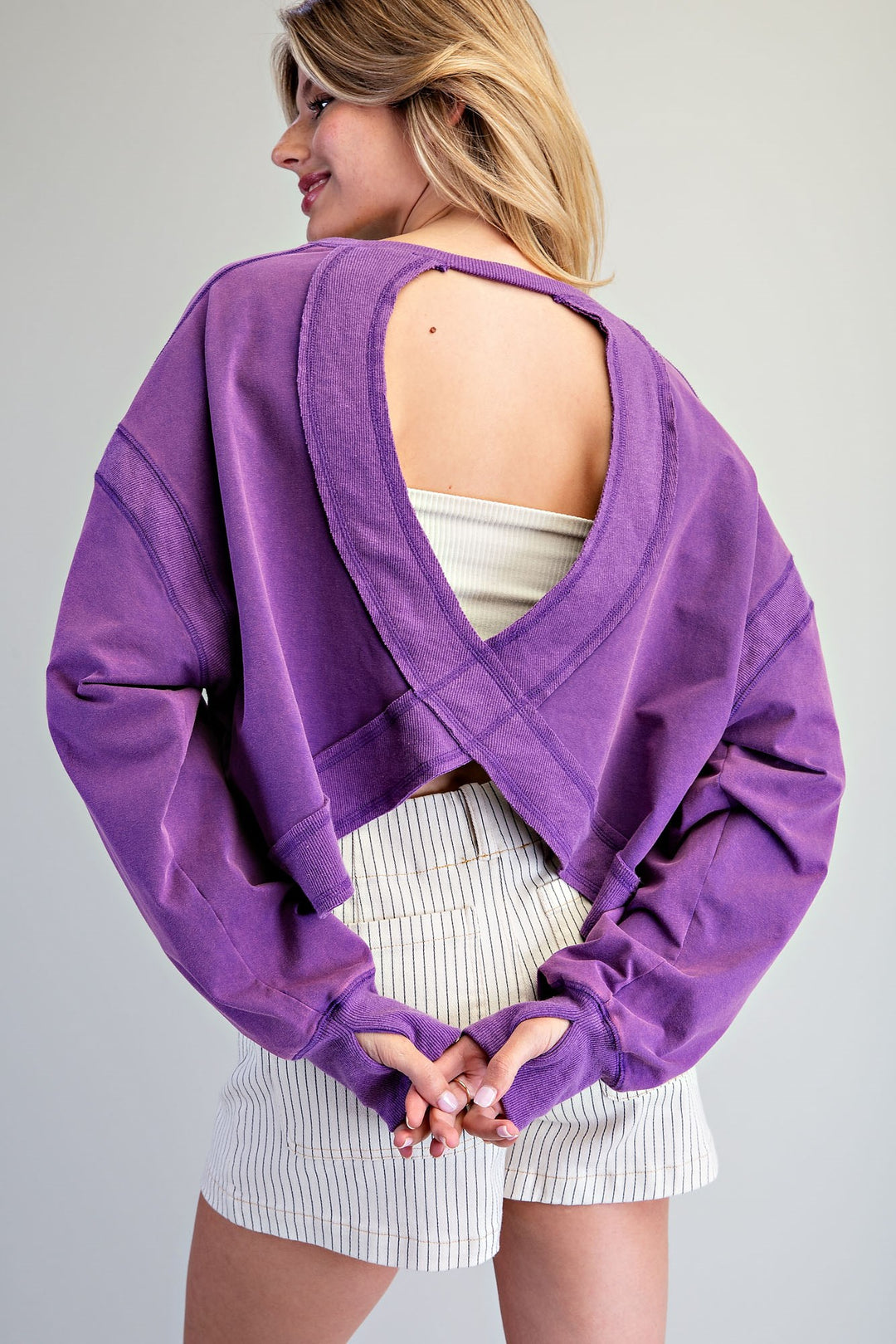 Person wearing a purple open-back sweatshirt against a gray background