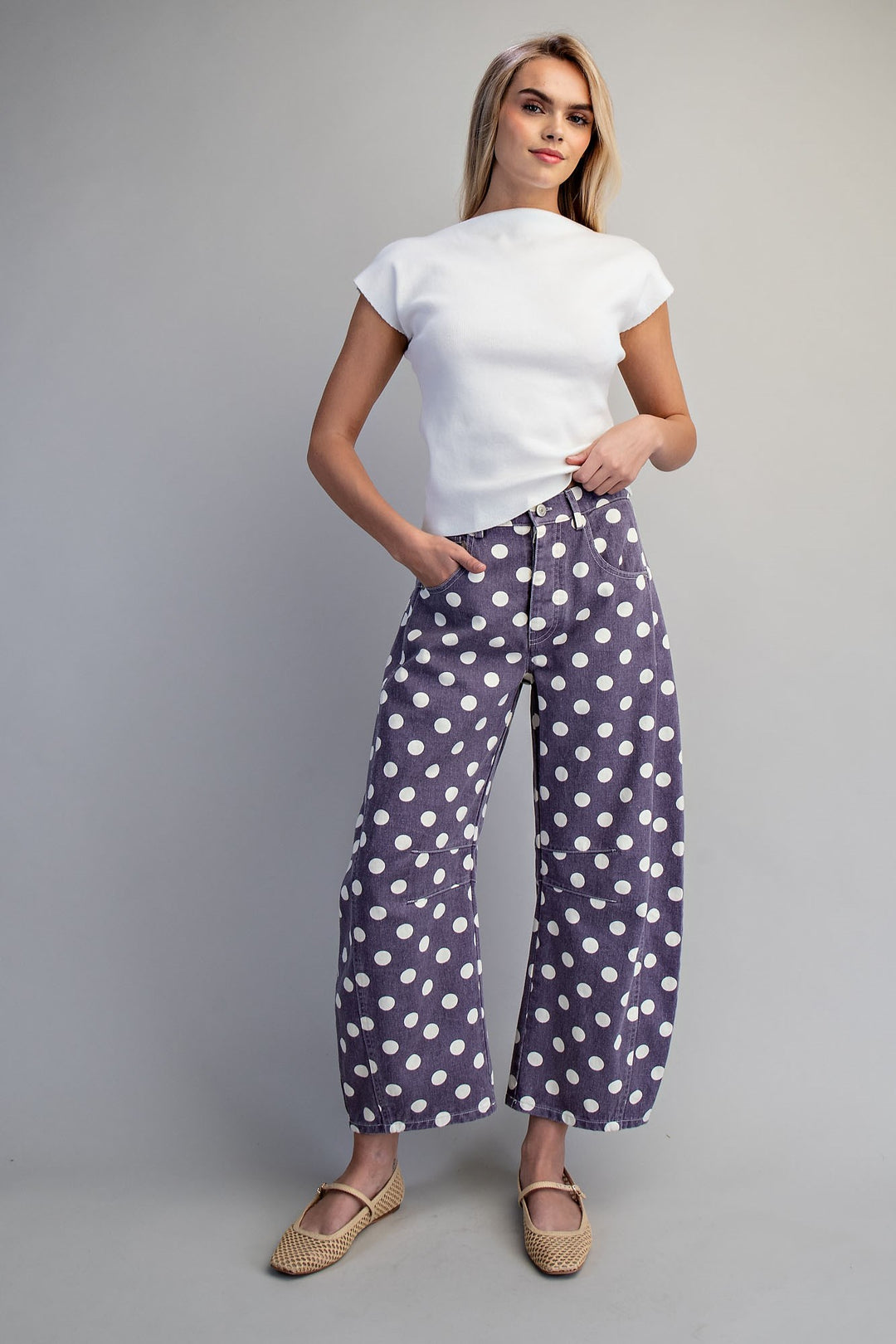 Woman wearing purple and white polka dot pants and white shirt on plain background