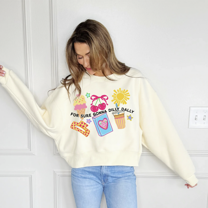 Woman wearing a cream sweatshirt with colorful graphics and text against a white wall.