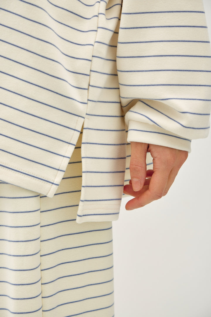 Close-up of a person wearing a cream-colored striped top and matching bottoms with thin blue horizontal stripes, showing the sleeve and hand.