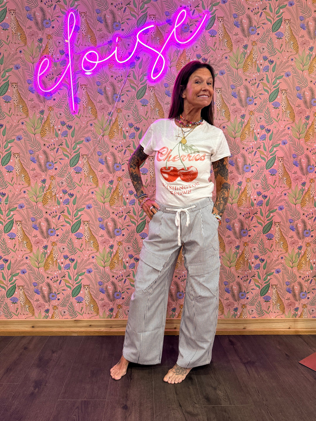 Woman wearing blue and white stripe pants and graphic tee on pink floral background