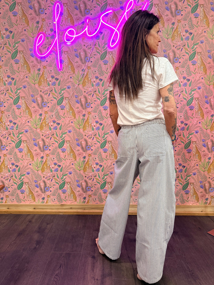 Back of woman wearing blue and white stripe pants and white tee on pink floral background
