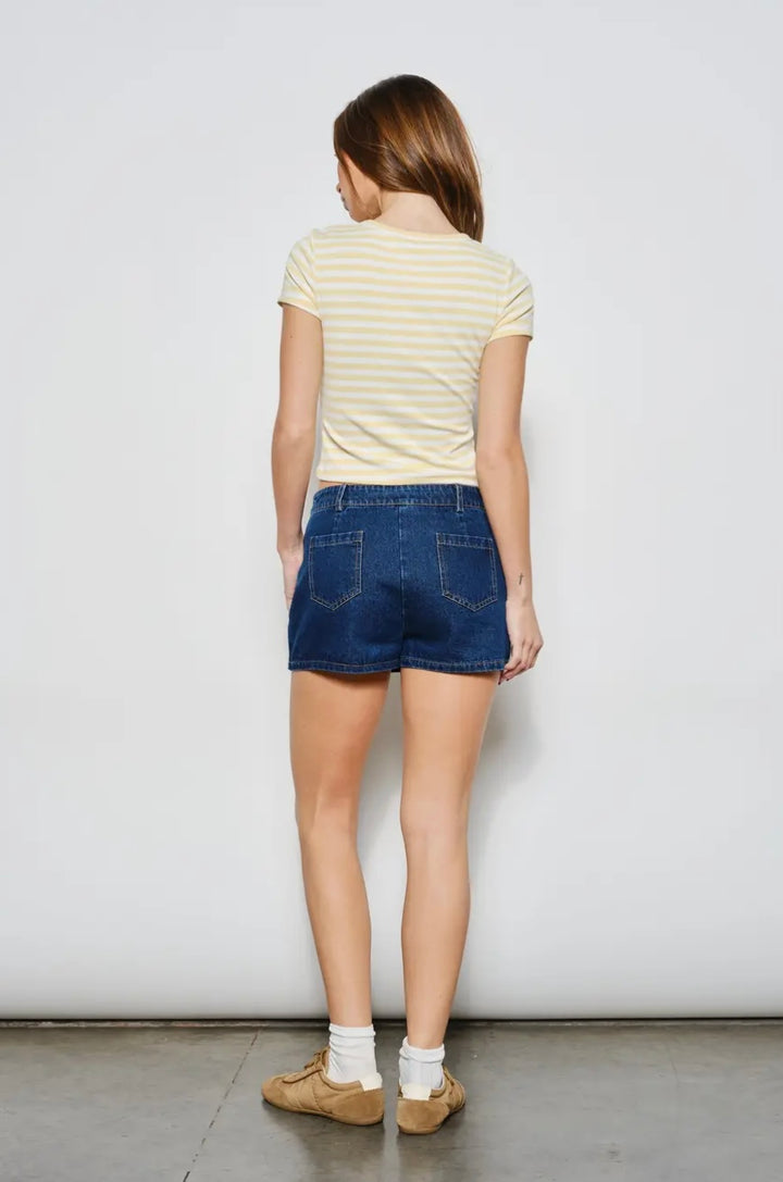 Person wearing a yellow striped shirt and blue denim shorts against a white wall.