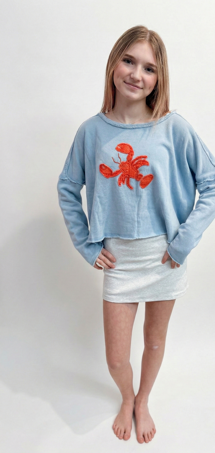 Young girl wearing a light blue sweatshirt with a red lobster design on a white background