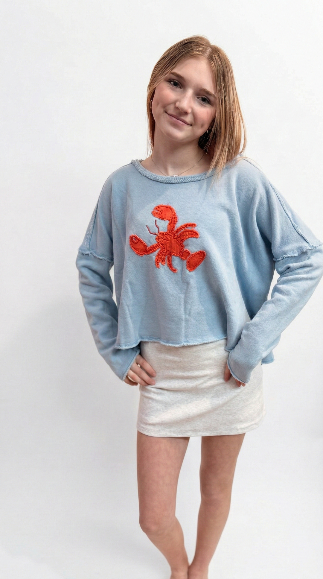 Woman wearing a light blue sweater with a red lobster design on a white background