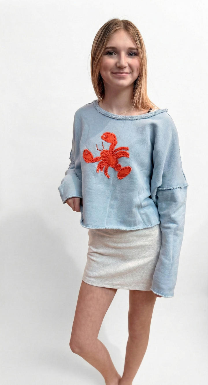 Woman wearing a light blue sweater with a red lobster design on a white background
