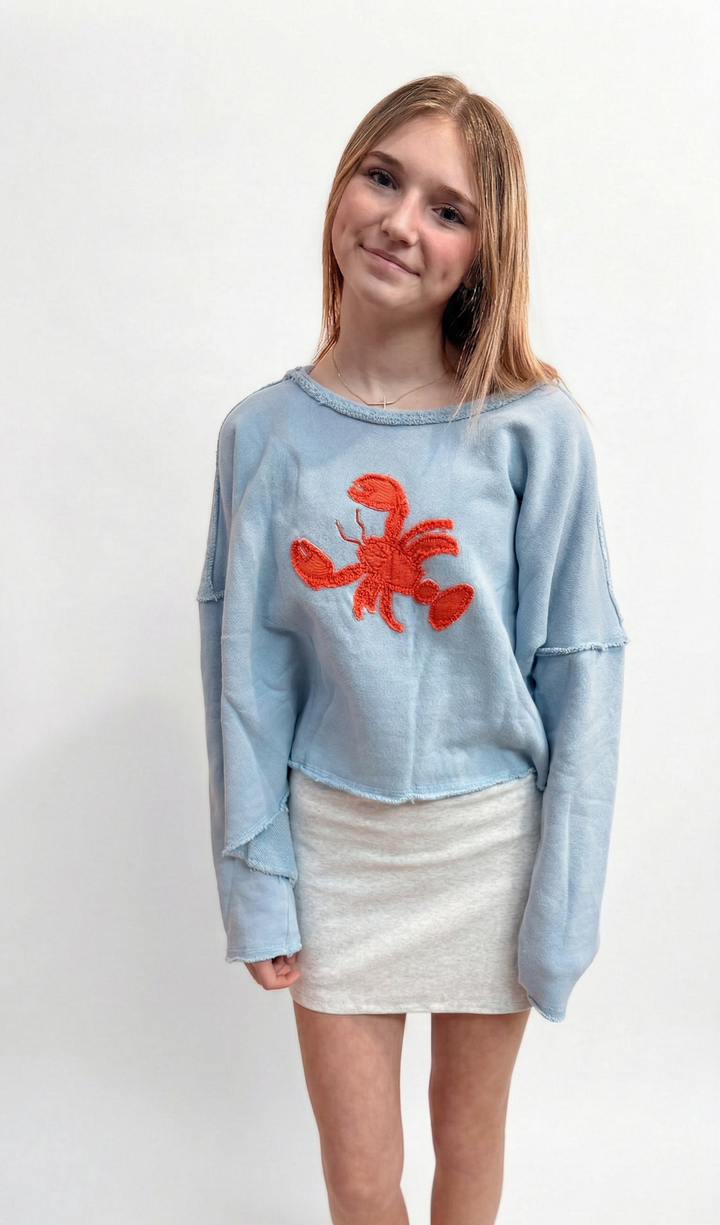 Girl wearing a light blue sweater with a red lobster design on a white background