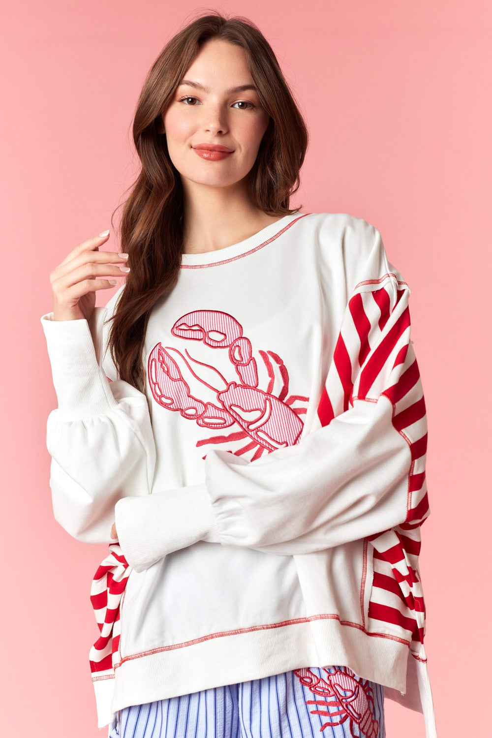 Woman wearing white and red stripe sweatshirt with lobster detail on pink background