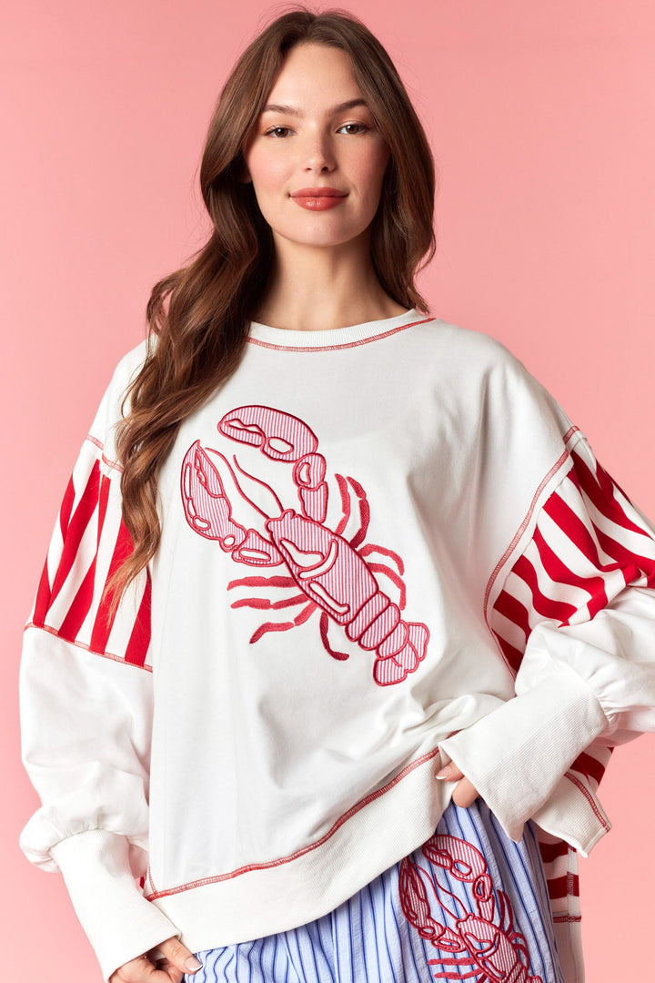 Woman wearing white and red stripe sweatshirt with lobster detail on pink background