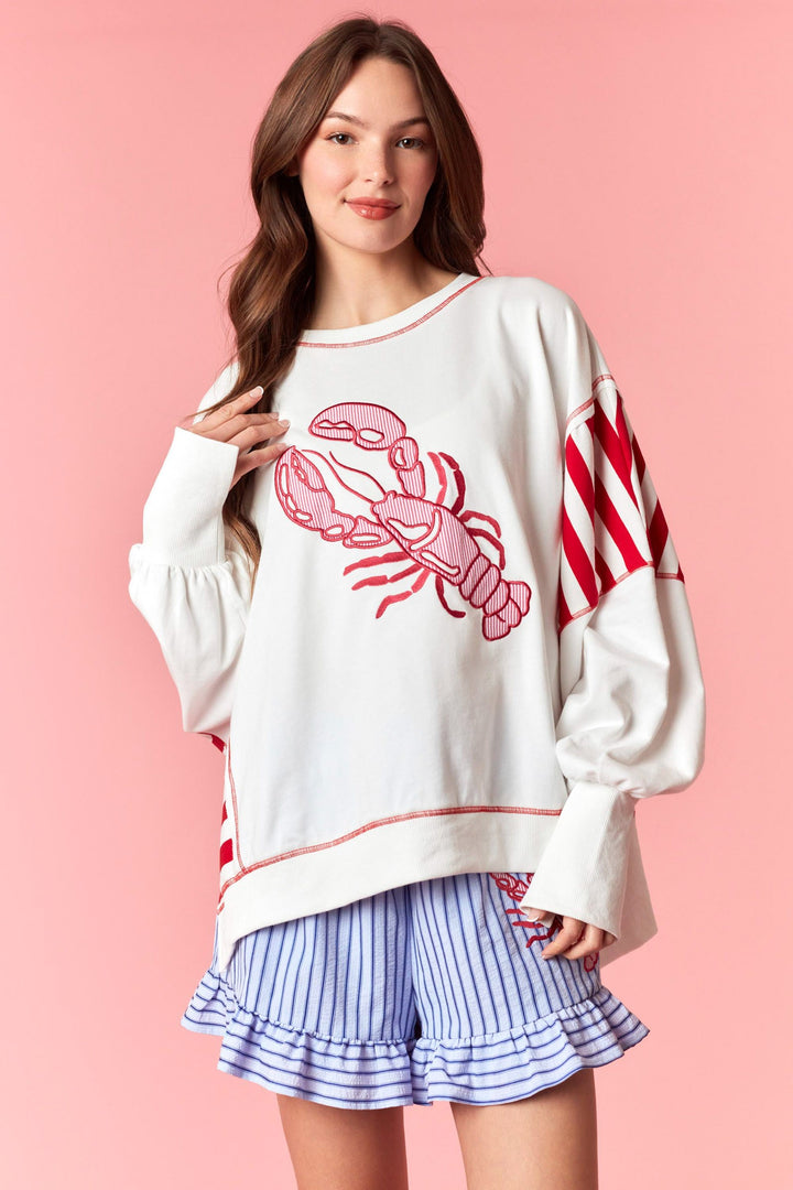 Woman wearing white and red stripe sweatshirt with lobster detail on pink background