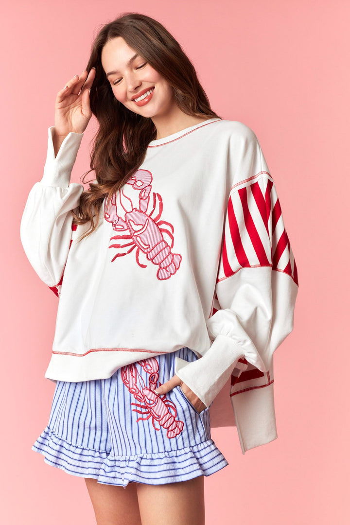 Woman wearing white and red stripe sweatshirt with lobster detail on pink background