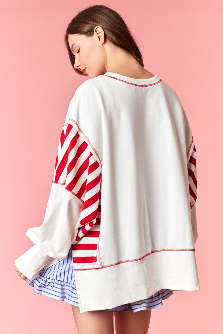 Back of woman wearing white and red stripe sweatshirt on pink background