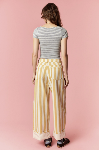 Woman wearing a striped shirt and yellow checkered pants against a pink background