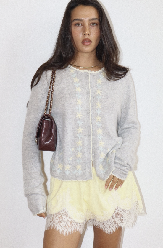 Woman wearing a light gray cardigan with star patterns and a yellow lace skirt on a white background