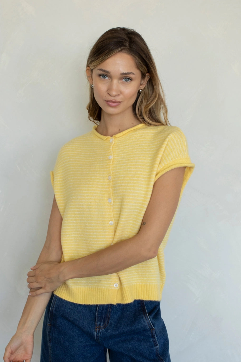 Woman wearing a yellow sleeveless cardigan against a plain background